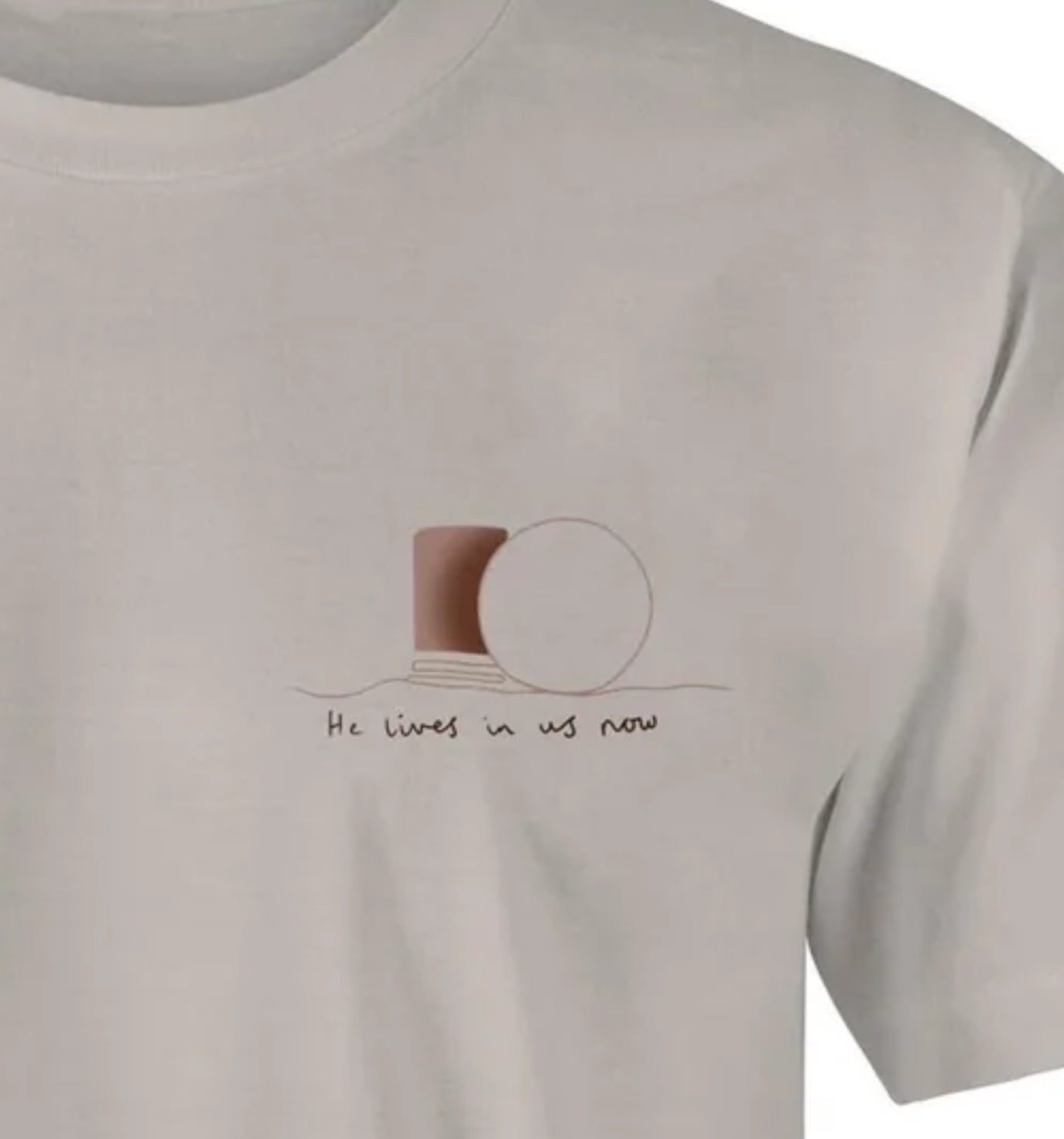 light brown t-shirt with graphic on left chest area depicting the stone rolled away from the tomb, with the words underneath "He lives in us now"